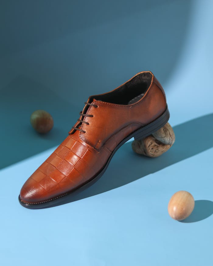 Studio shot of a stylish brown leather mens shoe on a blue backdrop with nuts.